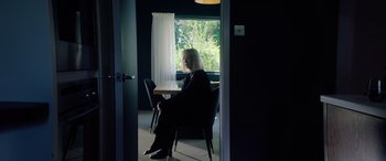Movie still from “A Banquet” (2021), directed by Ruth Paxton – A woman sitting at a table in front of a window; Medium shot, High angle