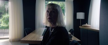 Movie still from “A Banquet” (2021), directed by Ruth Paxton – A woman sitting in front of a window in front of a table; Close Up shot, Low angle