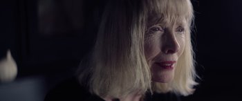 Movie still from “A Banquet” (2021), directed by Ruth Paxton – An older woman with blonde hair is smiling for the camera; Close Up shot, Low angle
