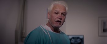 Movie still from “A Banquet” (2021), directed by Ruth Paxton – An older man in a hospital gown is looking at the camera; Close Up shot, Low angle