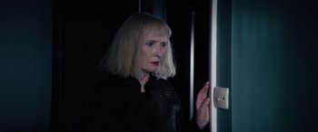 Movie still from “A Banquet” (2021), directed by Ruth Paxton – A woman in a black shirt standing in front of a door; Close Up shot, Low angle