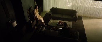 Movie still from “A Banquet” (2021), directed by Ruth Paxton – Two people sitting in a living room with a bowl of fruit on the table; Wide shot, High angle