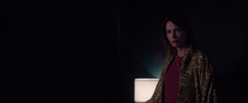 Movie still from “A Banquet” (2021), directed by Ruth Paxton – A woman standing in a dark room with a lamp; Medium shot, Over the shoulder angle