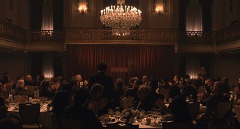 Movie still from “A Beautiful Day in the Neighborhood” (2019), directed by Marielle Heller – A group of people sitting at a table in front of a stage; Extreme Wide shot, High angle