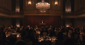 Movie still from “A Beautiful Day in the Neighborhood” (2019), directed by Marielle Heller – A group of people sitting at tables in front of a microphone; Extreme Wide shot, High angle