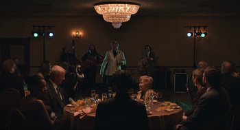 Movie still from “A Beautiful Day in the Neighborhood” (2019), directed by Marielle Heller – A group of people sitting at a table with a microphone; Wide shot, Over the shoulder angle
