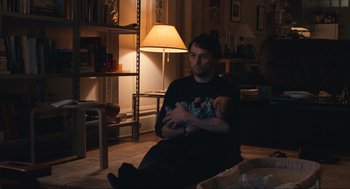 Movie still from “A Beautiful Day in the Neighborhood” (2019), directed by Marielle Heller – A man sitting on the floor holding a baby in his arms; Medium shot, Over the shoulder angle