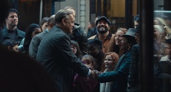 Movie still from “A Beautiful Day in the Neighborhood” (2019), directed by Marielle Heller – A group of people gathered around a man shaking hands; Medium shot, Over the shoulder angle