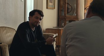 Movie still from “A Beautiful Day in the Neighborhood” (2019), directed by Marielle Heller – A man sitting in a living room holding a wii controller; Medium shot, Over the shoulder angle