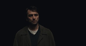 A man in a brown jacket is standing in the dark