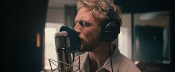 A man with a beard is listening to a microphone