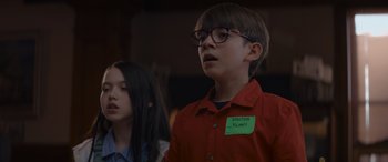 Movie still from “A Christmas Mystery” (2022), directed by Alex Ranarivelo – A boy wearing glasses and a red shirt is standing next to a girl wearing glasses; Close Up shot, Over the shoulder angle