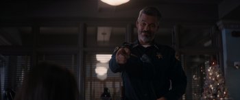 Movie still from “A Christmas Mystery” (2022), directed by Alex Ranarivelo – A man in a police uniform pointing at something; Medium shot, Over the shoulder angle