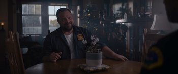 Movie still from “A Christmas Mystery” (2022), directed by Alex Ranarivelo – A man sitting at a table with a plant in front of him; Medium shot, Over the shoulder angle