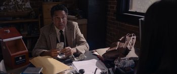 Movie still from “A Christmas Mystery” (2022), directed by Alex Ranarivelo – A man sitting at a table holding a stack of money; Medium shot, Over the shoulder angle