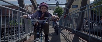 Movie still from “A Christmas Mystery” (2022), directed by Alex Ranarivelo – Two people riding bicycles down a bridge; Medium shot, Low angle