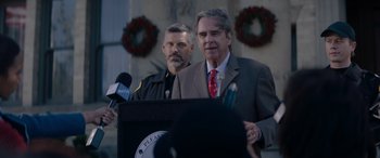 Movie still from “A Christmas Mystery” (2022), directed by Alex Ranarivelo – A man in a suit and tie standing next to another man in a suit and tie holding microphones; Close Up shot, Over the shoulder angle
