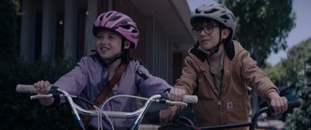 Movie still from “A Christmas Mystery” (2022), directed by Alex Ranarivelo – Two young girls wearing helmets on a bicycle; Close Up shot, Over the shoulder angle