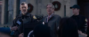 Movie still from “A Christmas Mystery” (2022), directed by Alex Ranarivelo – A man in a suit and tie speaking at a podium; Close Up shot, Over the shoulder angle