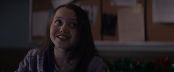 Movie still from “A Christmas Mystery” (2022), directed by Alex Ranarivelo – A young girl smiles brightly while sitting in a room; Close Up shot, Over the shoulder angle