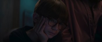 Movie still from “A Christmas Mystery” (2022), directed by Alex Ranarivelo – A boy with glasses is looking at the camera with his hand on his face; Close Up shot, High angle