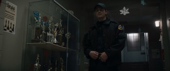 Movie still from “A Christmas Mystery” (2022), directed by Alex Ranarivelo – A man standing in front of a display case of trophies; Medium shot, Low angle