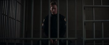 Movie still from “A Christmas Mystery” (2022), directed by Alex Ranarivelo – A police officer sitting behind bars in a jail cell; Medium shot, Low angle