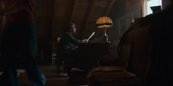 Movie still from “A Christmas Story Christmas” (2022), directed by Clay Kaytis – A man sitting at a desk in a room with a lamp; Wide shot, Low angle
