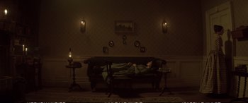 Movie still from “Emily” (2022), directed by Frances O'Connor – A person laying on a couch in a living room; Wide shot, High angle