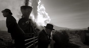Movie still from “The Fall” (2006), directed by Tarsem Singh – A man in a suit and hat standing in front of a steam train; Wide shot, Low angle