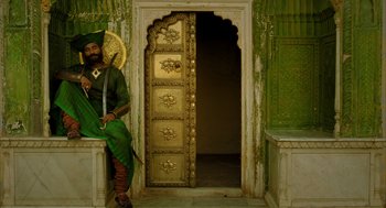 Movie still from “The Fall” (2006), directed by Tarsem Singh – A man sitting on a bench in front of a door; Wide shot, Low angle