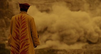 Movie still from “The Fall” (2006), directed by Tarsem Singh – A man in a yellow coat standing in front of a wall of smoke; Wide shot, Over the shoulder angle