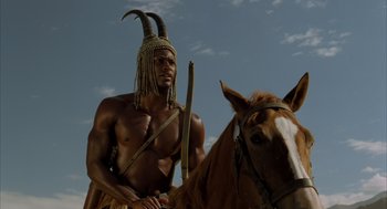 A man with a spear standing next to a brown horse