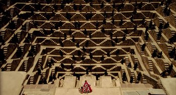 Movie still from “The Fall” (2006), directed by Tarsem Singh – A man sitting on steps in front of an audience; Extreme Wide shot, Overhead angle