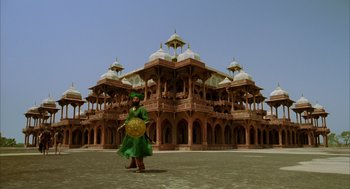 Movie still from “The Fall” (2006), directed by Tarsem Singh – A woman in a green dress standing in front of a building; Extreme Wide shot, Low angle