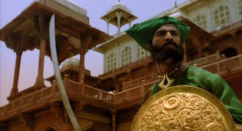Movie still from “The Fall” (2006), directed by Tarsem Singh – A man with a beard wearing a green turban and holding a shield; Medium shot, Low angle