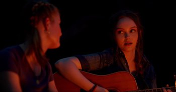 Movie still from “A Cowgirl's Song” (2022), directed by Timothy Armstrong – A woman sitting next to another woman holding a guitar; Close Up shot, Over the shoulder angle
