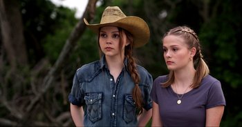 Movie still from “A Cowgirl's Song” (2022), directed by Timothy Armstrong – Two young women standing next to each other in a park; Close Up shot, Over the shoulder angle
