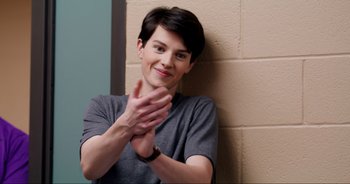 Movie still from “A Cowgirl's Song” (2022), directed by Timothy Armstrong – A woman sitting against a wall clapping her hands; Medium shot, Over the shoulder angle