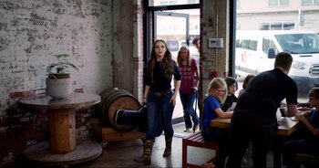 Movie still from “A Cowgirl's Song” (2022), directed by Timothy Armstrong – A woman standing next to a barrel in a room; Wide shot, Over the shoulder angle