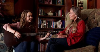 Movie still from “A Cowgirl's Song” (2022), directed by Timothy Armstrong – A woman sitting next to a woman holding a guitar; Medium shot, Over the shoulder angle