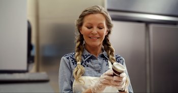 Movie still from “A Cowgirl's Song” (2022), directed by Timothy Armstrong – A woman holding a jar of food while wearing a white apron; Close Up shot, Over the shoulder angle