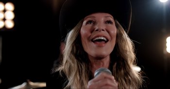 Movie still from “A Cowgirl's Song” (2022), directed by Timothy Armstrong – A person holding a microphone and wearing a hat; Close Up shot, Low angle