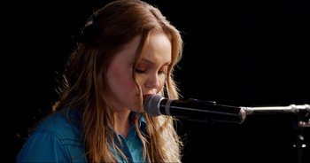 Movie still from “A Cowgirl's Song” (2022), directed by Timothy Armstrong – A woman with long hair is singing into a microphone; Close Up shot, Over the shoulder angle