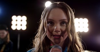 Movie still from “A Cowgirl's Song” (2022), directed by Timothy Armstrong – A woman with long hair is holding a microphone; Close Up shot, Over the shoulder angle