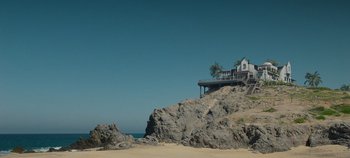Movie still from “A Deadly Invitation” (2023), directed by J.M Cravioto – A house sitting on top of a rock on the beach; Extreme Wide shot, Low angle