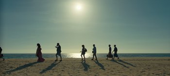 Movie still from “A Deadly Invitation” (2023), directed by J.M Cravioto – A group of people walking along the beach; Extreme Wide shot, Low angle
