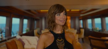 Movie still from “A Deadly Invitation” (2023), directed by J.M Cravioto – A woman in a black dress is smiling for the camera; Medium shot, Over the shoulder angle