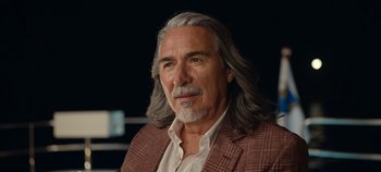 Movie still from “A Deadly Invitation” (2023), directed by J.M Cravioto – An older man with long grey hair wearing a suit; Close Up shot, Over the shoulder angle