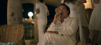 Movie still from “A Deadly Invitation” (2023), directed by J.M Cravioto – A man in a white suit smoking a cigarette; Medium shot, Low angle